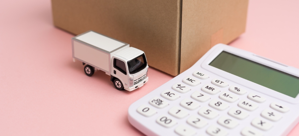 calculatrice à côté d'un camion miniature et d'un carton de déménagement, sur fond rose