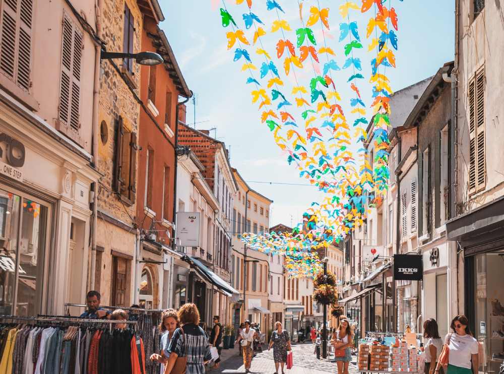 Vue de la rue du Maréchal Foch à Roanne, un jour ensoleillé, avec des guirlandes de papillons suspendues.